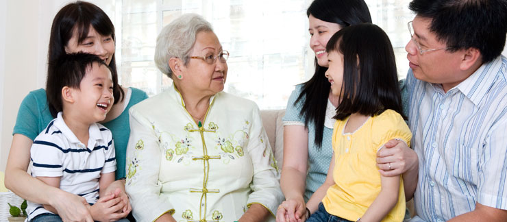 Senior woman sits on couch surrounded by family, including smiling grandchildren.