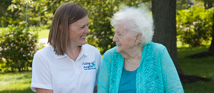 A female in-home care provider walks outside with an elderly woman who has dementia.