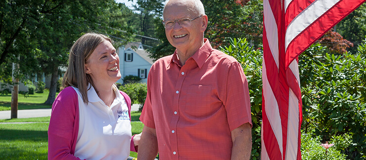 Female care worker stands next to an American flag with a smiling elderly man.