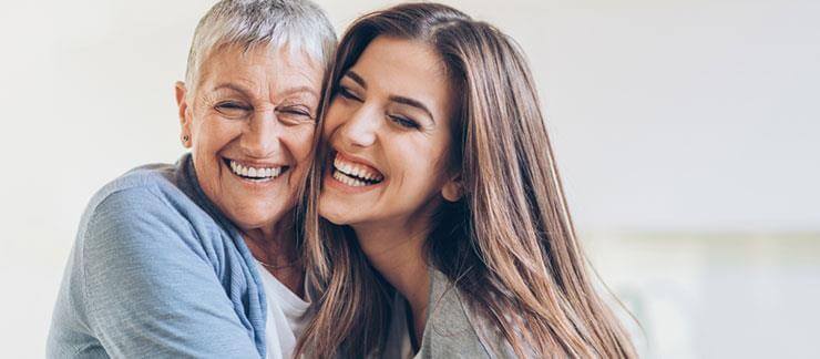 Senior woman smiles while hugging adult daughter during a visit at her home.