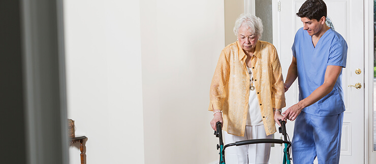 Elderly woman with walker receives support at home from male care provider.