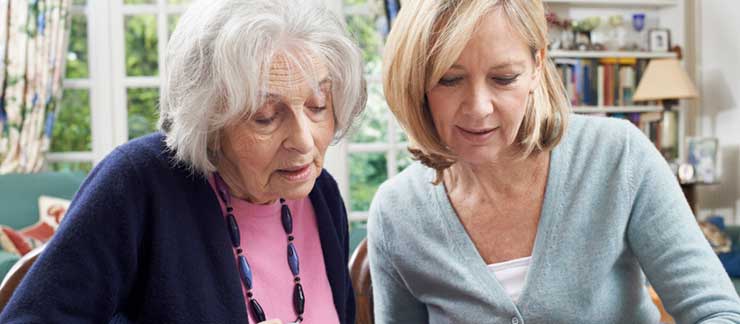 An adult woman and an elderly woman sit side by side at a table both examining the document laying in front of them